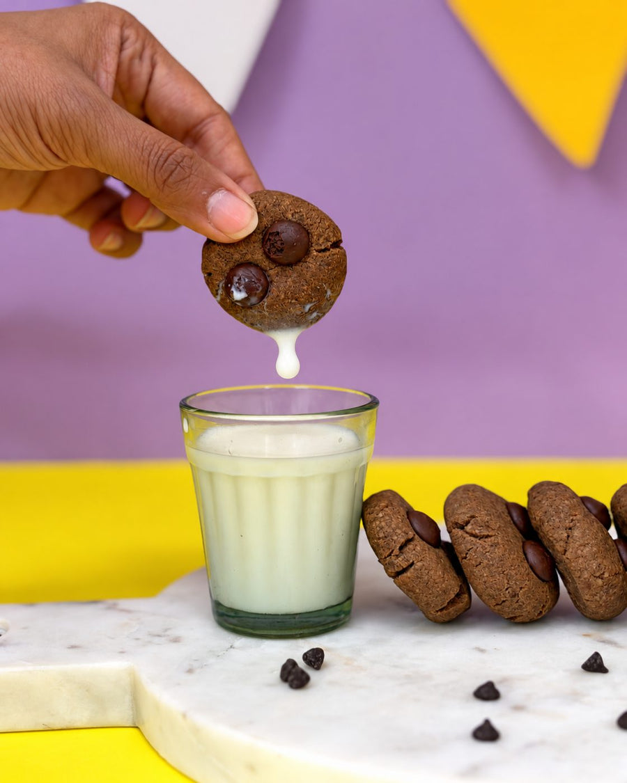 Hand dunking a ragi chocolate cookie into a glass of milk